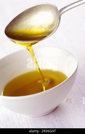 Olio d'oliva che scorre da un cucchiaio in una ciotola Foto Stock