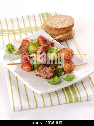 Salsicce avvolto in pancetta e cavoletti di Bruxelles su spiedini Foto Stock