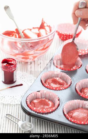 Pastella di torta di velluto rosso che è riempita in casse di cupcake di carta Foto Stock