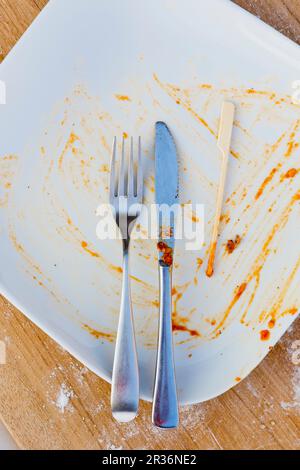 Un piatto vuoto con posate, uno spiedino di legno e i resti di salsa Foto Stock