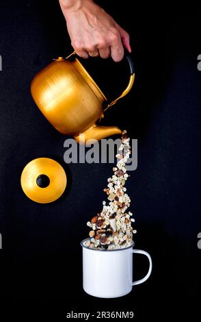 Muesli versata da una teiera in uno smalto mug Foto Stock