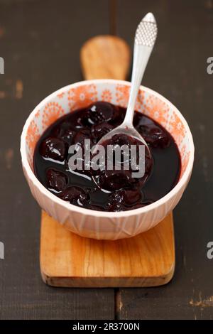 Marmellata di ciliegie in una ciotola su un tagliere Foto Stock