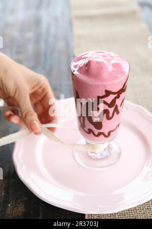 Un frullato di lampone e cioccolato in un bicchiere decorato con nastro Foto Stock