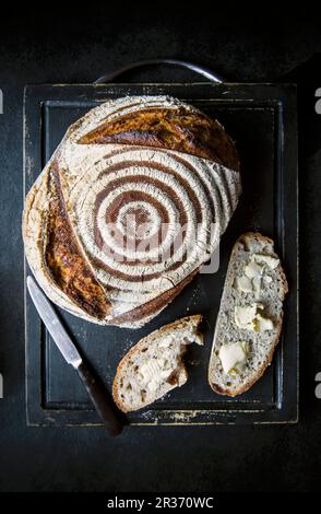 Una pagnotta appena sfornata di pane a pasta madre e due fette di burro Foto Stock