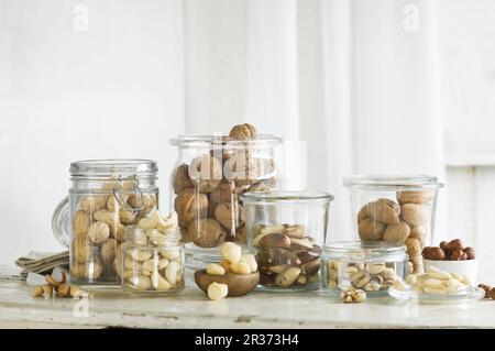 Vari tipi di noci in vasetti di vetro su un tavolo da cucina rustico Foto Stock