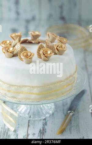 Una torta bianca festosa con rose d'oro e nastro decorativo Foto Stock