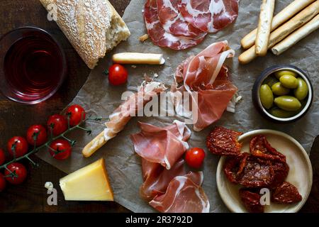 Antepasto italiani sparsi su cera rugosa di carta e legno scuro board Foto Stock