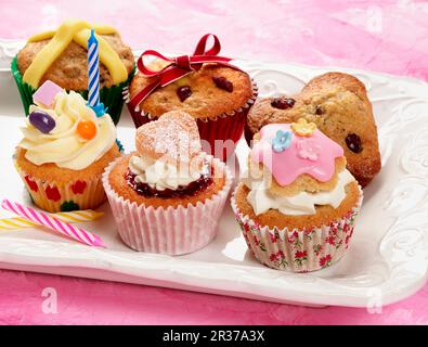 Una selezione di diversi cupcake da festa su un piatto di crema e sfondo rosa Foto Stock