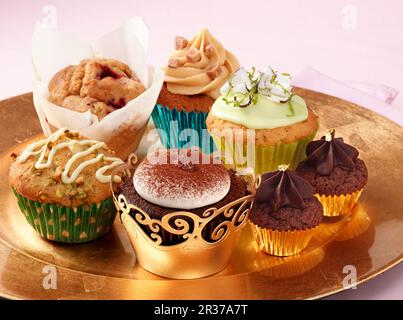 Una selezione di diversi cupcake di lusso su un piatto d'oro su sfondo rosa Foto Stock