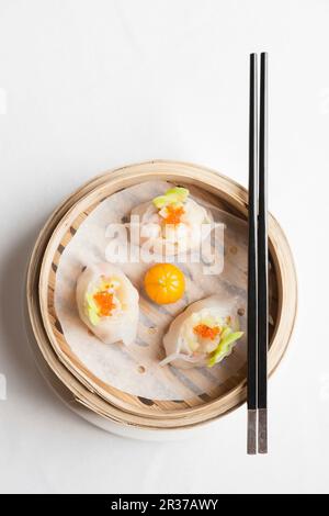 Gnocchi cinesi al vapore con gamberi e crostini di pesce in un cestino di bambù con bastoncini Foto Stock