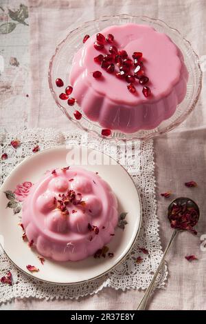 Due rosa pastello gelatine di latte sul vetro vintage cake stand e la piastra una coperta con semi pomegrante gli altri con secchi petali di rosa shot overhead sul Foto Stock