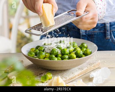 Un uomo di grattugiare il formaggio su brussel germogli di Dell Foto Stock