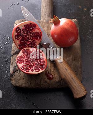 Due melograni, interi e tagliati a metà, con un coltello su un vecchio asse di legno Foto Stock