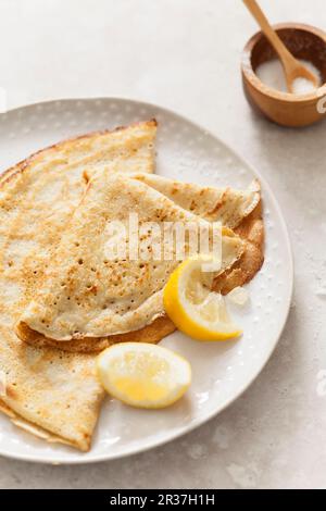 Due frittelle piegate su un piatto di consistenza biancastra con spicchi di limone su una superficie di pietra Foto Stock