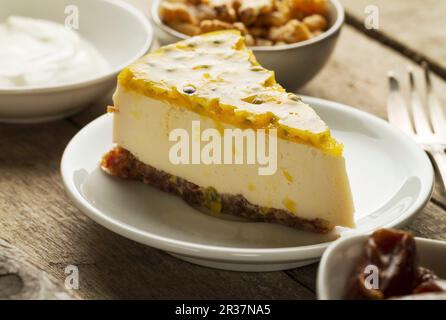 Una fetta di mascarpone e yogurt greco cheesecake con una data e una base in legno di noce, guarnita con maracuja Foto Stock