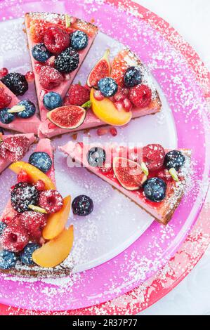 Vista dall'alto delle fette di cheesecake alle fragole su tre piatti rosa e rosso sormontati da frutta fresca e coulis alle fragole Foto Stock
