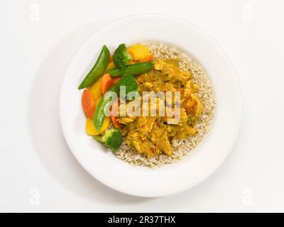 Masala di pollo con verdure e riso su un piatto di fronte a uno sfondo bianco Foto Stock