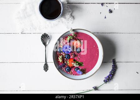 Una ciotola di frullato con frutta, fiori commestibili e muesli senza glutine (visti dall'alto) Foto Stock