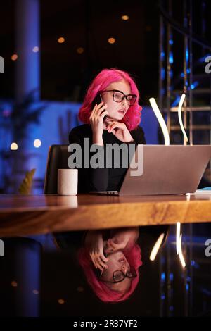 Giovane donna d'affari che lavora a tarda notte, bevendo caffè e parlando al telefono Foto Stock