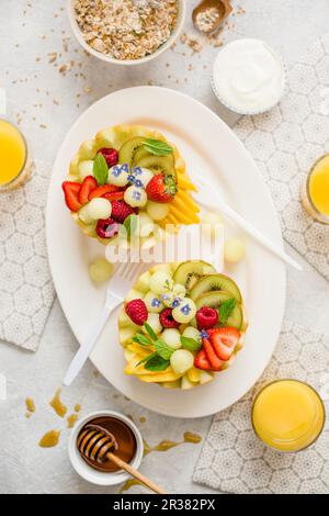 Una sana colazione: Macedonia di frutta servita a metà melone, yogurt, muesli, succo d'arancia e miele Foto Stock