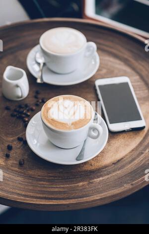 Due tazze di cappuccino accanto a uno smartphone su un tavolo in un bar Foto Stock