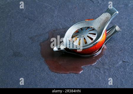 Mezzo arancio di sangue in una spremitoio da succo su sfondo grigio Foto Stock