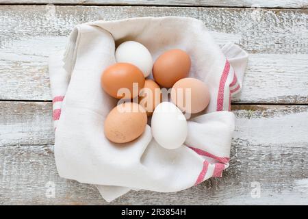 Uova di pollo in un tovagliolo da tè su uno sfondo di legno (visto dall'alto) Foto Stock
