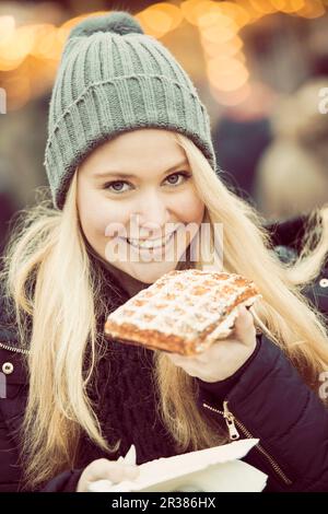 Una giovane donna vestita per l'inverno di mangiare una torta di mele in un mercato di Natale Foto Stock