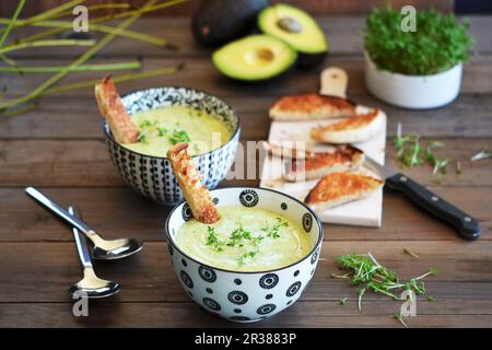 Zuppa di avocado in due ciotole su un tavolo rustico con pane tostato e stress fresco Foto Stock