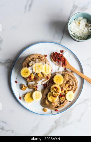 Frittelle di farro vegano con banane, bacche di goji e cocco Foto Stock