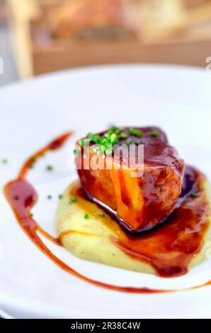 Pancia di maiale iberico brasata con sugo su un letto di purè di patate Foto Stock