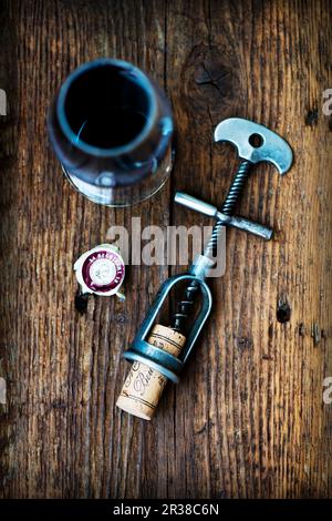 Un antico cavatappi con sughero e un bicchiere di vino rosso su una superficie di legno Foto Stock