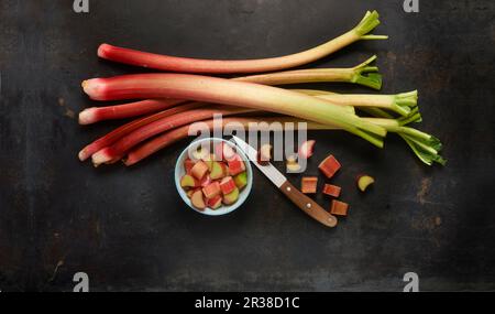 Steli di rabarbaro e di rabarbaro tagliato in una ciotola con un coltello Foto Stock