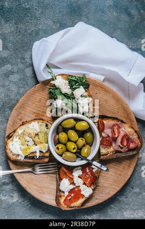 Bruschette e olive varie su un piatto di legno Foto Stock