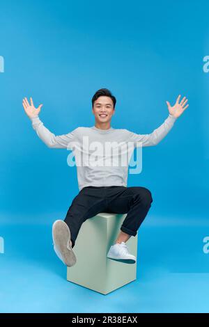 Casual giovane uomo seduto su una colonna di menta isolato su sfondo blu Foto Stock