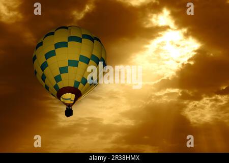 Mongolfiera in volo in un cielo nuvoloso di prima mattina, con luce del sole che splende sulla mongolfiera. Foto Stock