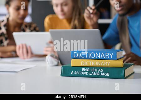 Primo piano di pile di libri sdraiati sul tavolo con studenti che studiano lingua straniera in background Foto Stock