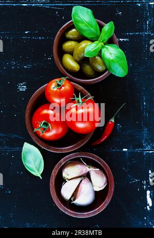 Ciotole di legno con olive verdi, pomodori ciliegini e aglio su fondo vintage scuro Foto Stock