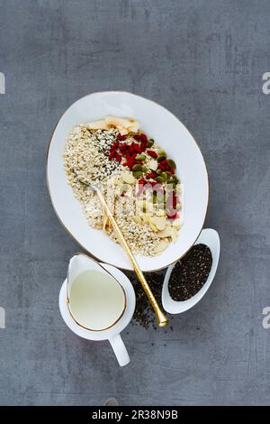 Primo piano di gustosi fiocchi di quinoa biologica e ingredienti sani per la colazione - latte, fiocchi di cocco, frutta secca, semi e noci su sfondo grigio Foto Stock