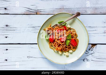 Pasta tradizionale italiana spaghetti con pomodori arrostiti, basilico fresco e parmigiano su piatto su fondo bianco rustico di legno Foto Stock