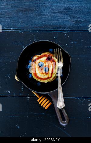 Vista dall'alto dei mirtilli pancake fatti in casa con miele e frutti di bosco freschi per colazione in una teglia di ghisa d'epoca su uno sfondo rustico in legno Foto Stock