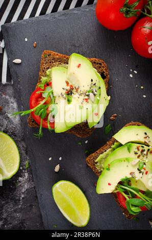 Toast all'avocado con pomodoro, snack salutare o colazione su sfondo nero scuro Foto Stock