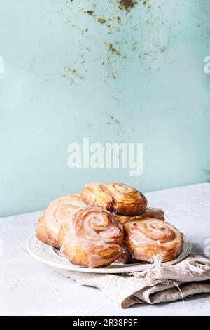 Piatto di pasta sfoglia smaltata fatta in casa dolci alla cannella su un panno sopra il tavolo grigio Foto Stock