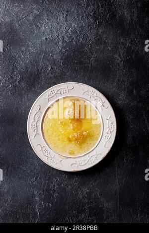 Nido d'ape in miele liquido su piatto bianco vintage su sfondo nero texture Foto Stock