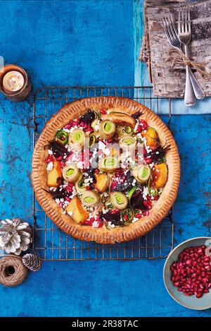 La torta di Natale vegetariana con nastri di zucchine, zucca alle butternut, barbabietole e porri, sormontata da feta e semi di melograno Foto Stock