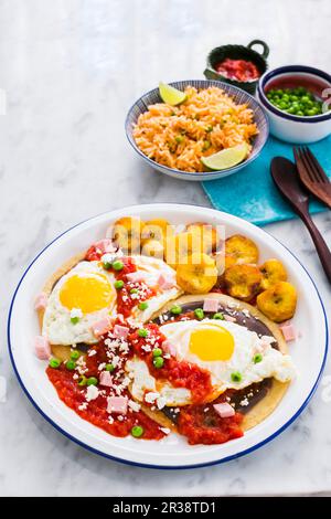 Huevos Motuleños (uova fritte su una tortilla con purea di fagioli neri, salsa al peperoncino, plantane, pancetta e formaggio, Messico) Foto Stock