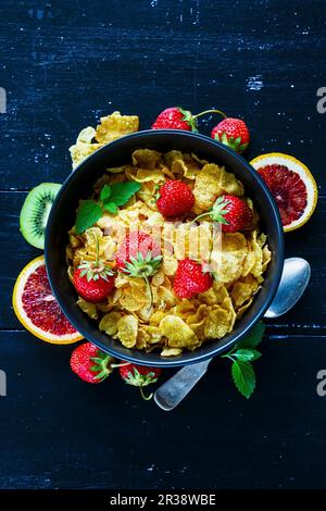 Primo piano del tavolo vintage con un sano set per la colazione. Cereali di mais, fragole fresche e frutta sullo sfondo di legno rustico scuro Foto Stock