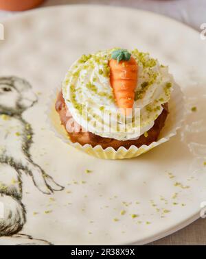 Un cupcake alla carota con crema di burro, pistacchi e una carota marzapane Foto Stock