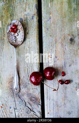 Ciliegie, semi di melograno e un vecchio cucchiaio su fondo di legno Foto Stock