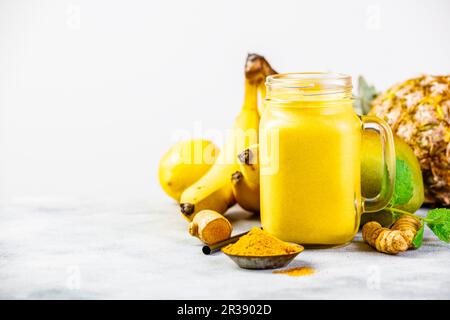 Frullato di frutta gialla con curcuma e ingredienti su un tavolo Foto Stock